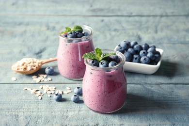 Photo of Tasty blueberry smoothie in jars, berries and oatmeal on wooden table