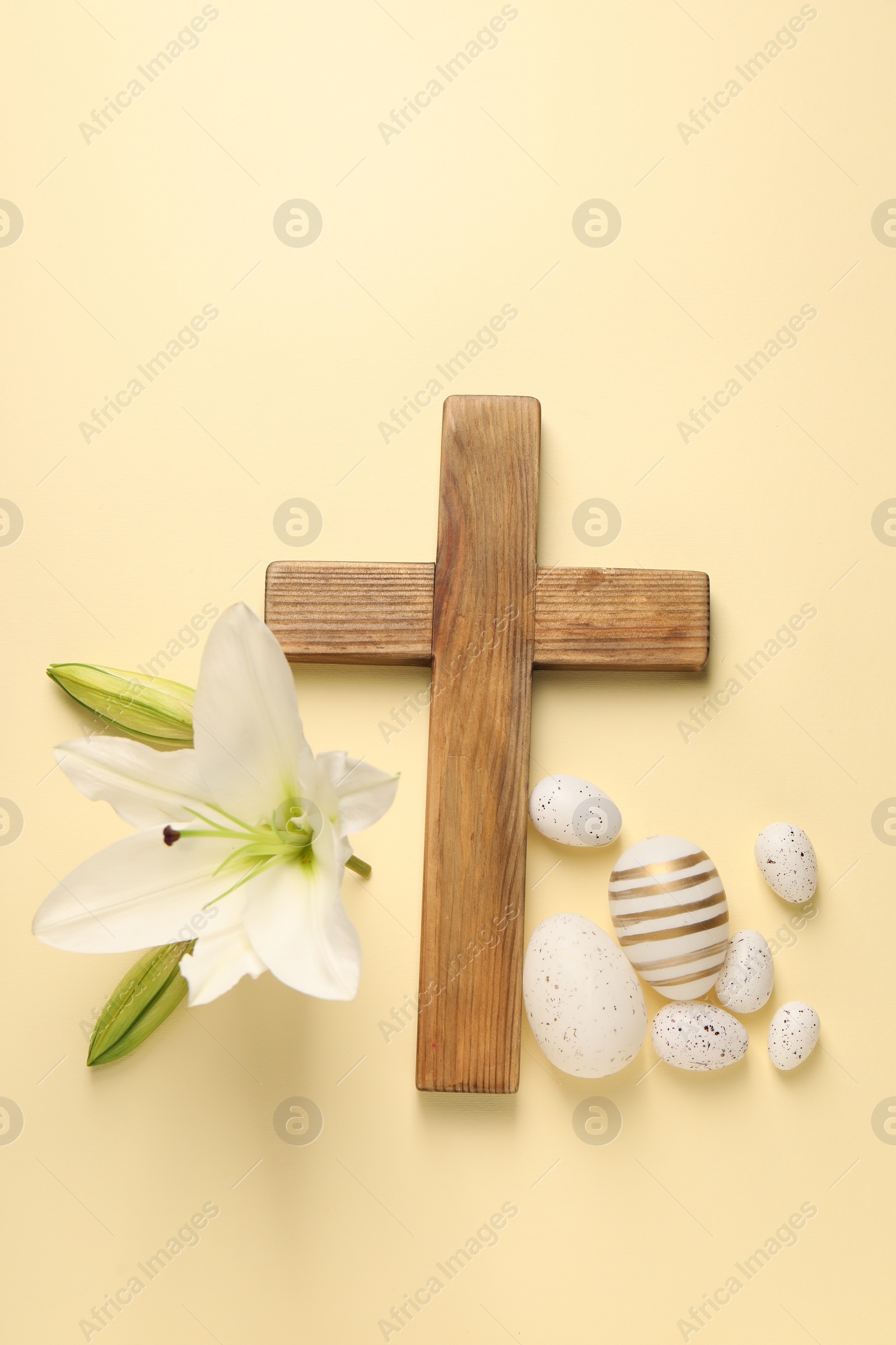 Photo of Wooden cross, painted Easter eggs and lily flowers on pale yellow background, flat lay