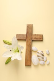 Wooden cross, painted Easter eggs and lily flowers on pale yellow background, flat lay