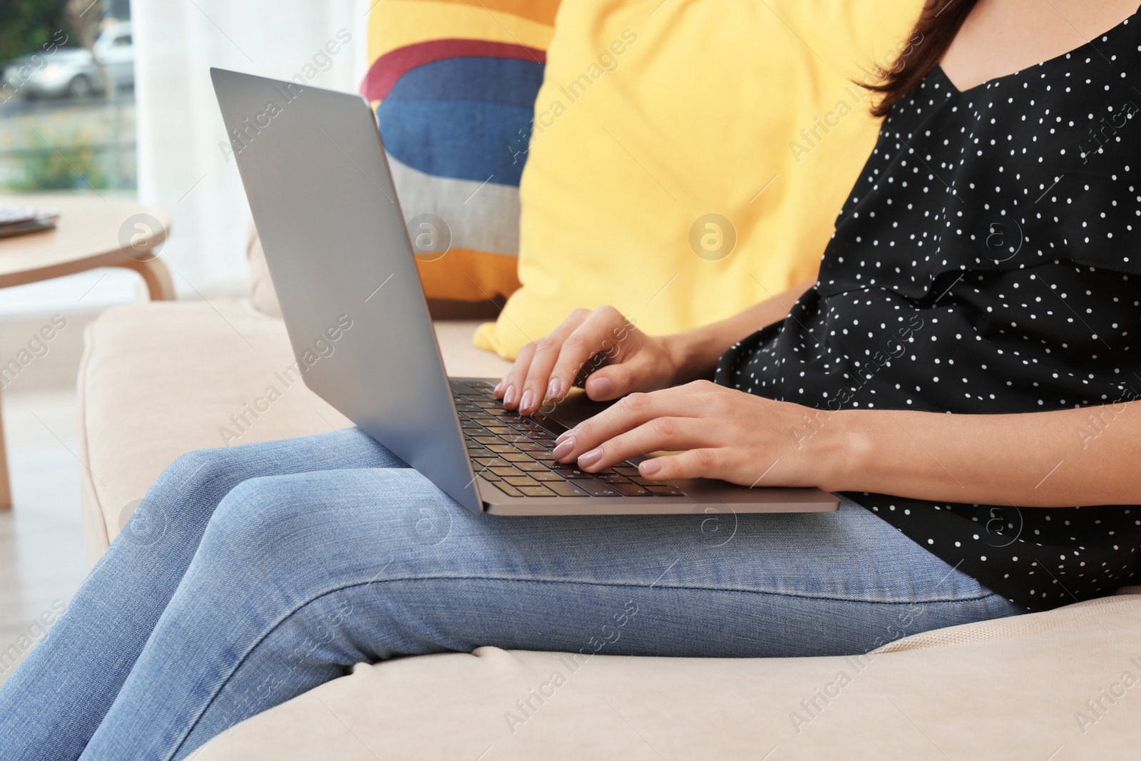 Photo of Young woman with modern laptop sitting on sofa at home, closeup