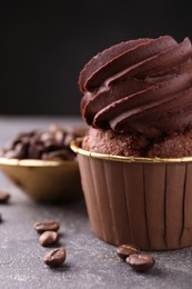 Delicious chocolate cupcake and coffee beans on grey textured table, closeup