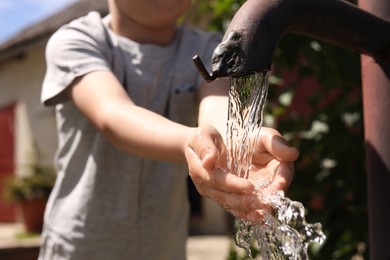 Water scarcity. Little boy drawing water with hands from tap outdoors, closeup