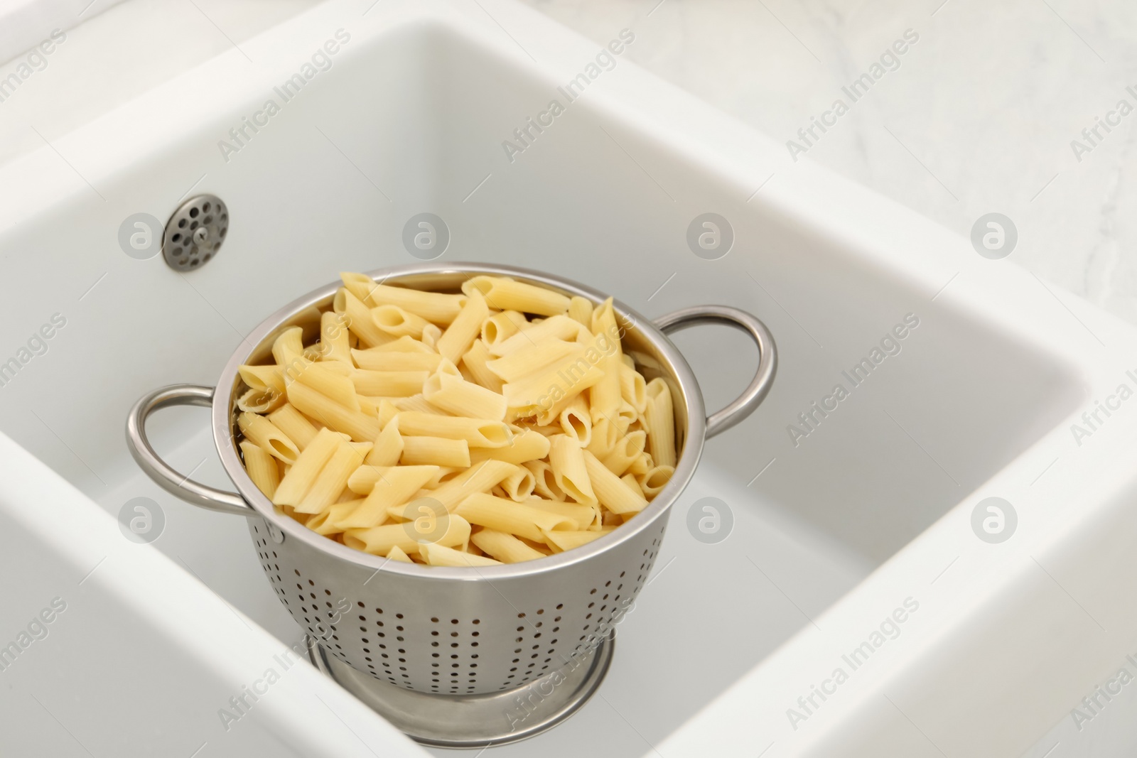 Photo of Metal colander with cooked pasta in sink