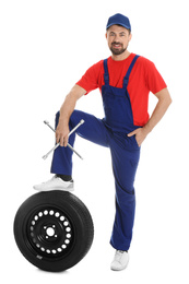 Full length portrait of professional auto mechanic with lug wrench and wheel on white background
