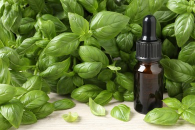 Photo of Glass bottle of basil essential oil and leaves on white wooden table. Space for text