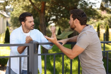Photo of Angry neighbours having argument near fence outdoors