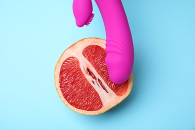 Photo of Half of grapefruit and purple vibrator on blue background, flat lay. Sex concept