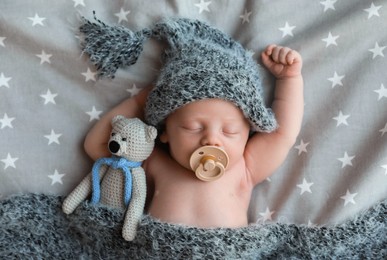 Cute newborn baby in warm hat with toy sleeping on bed, top view
