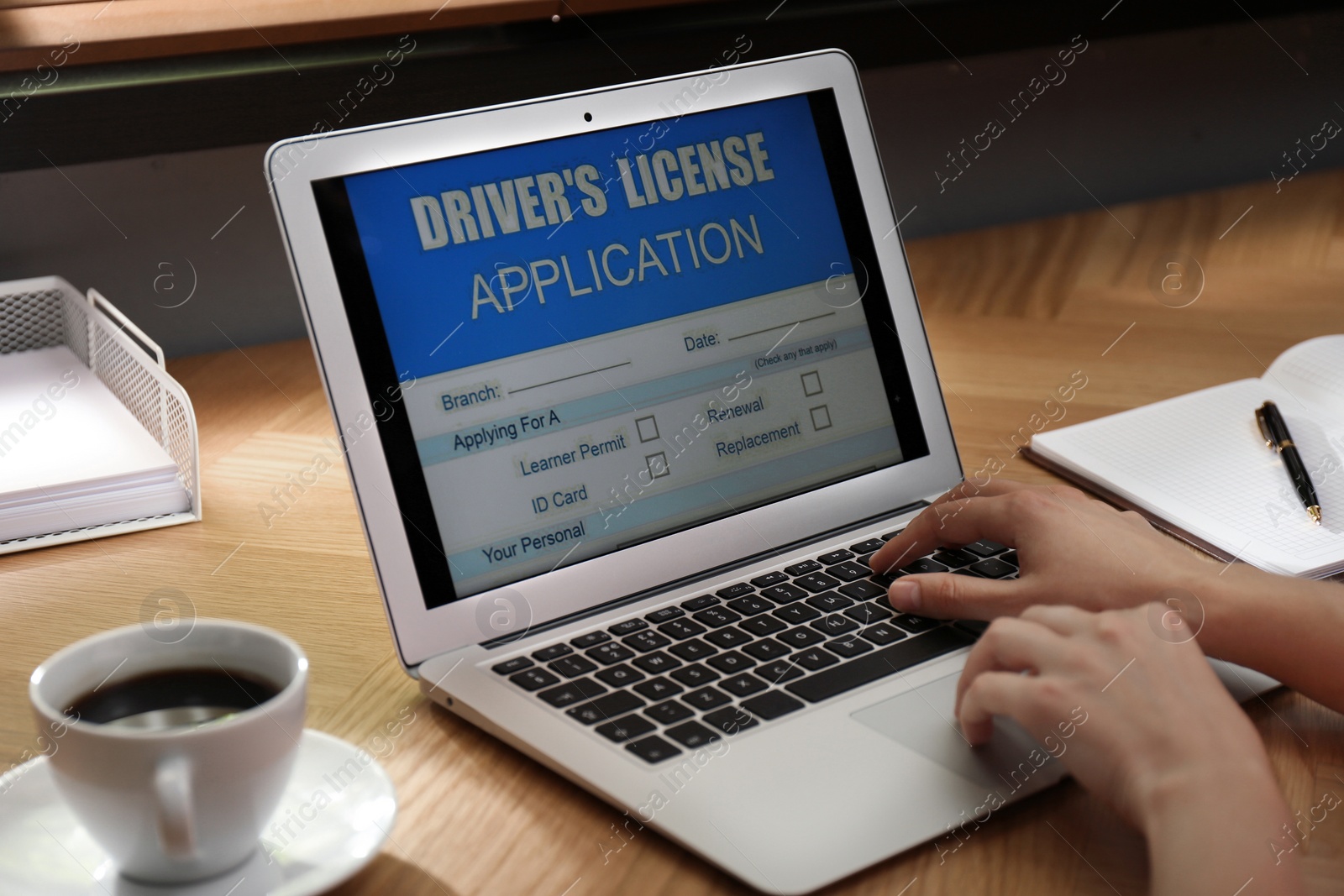 Photo of Woman using laptop to fill driver's license application form at table in office, closeup