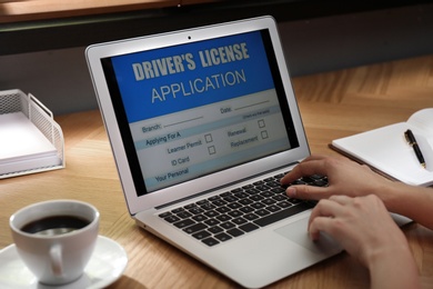 Photo of Woman using laptop to fill driver's license application form at table in office, closeup