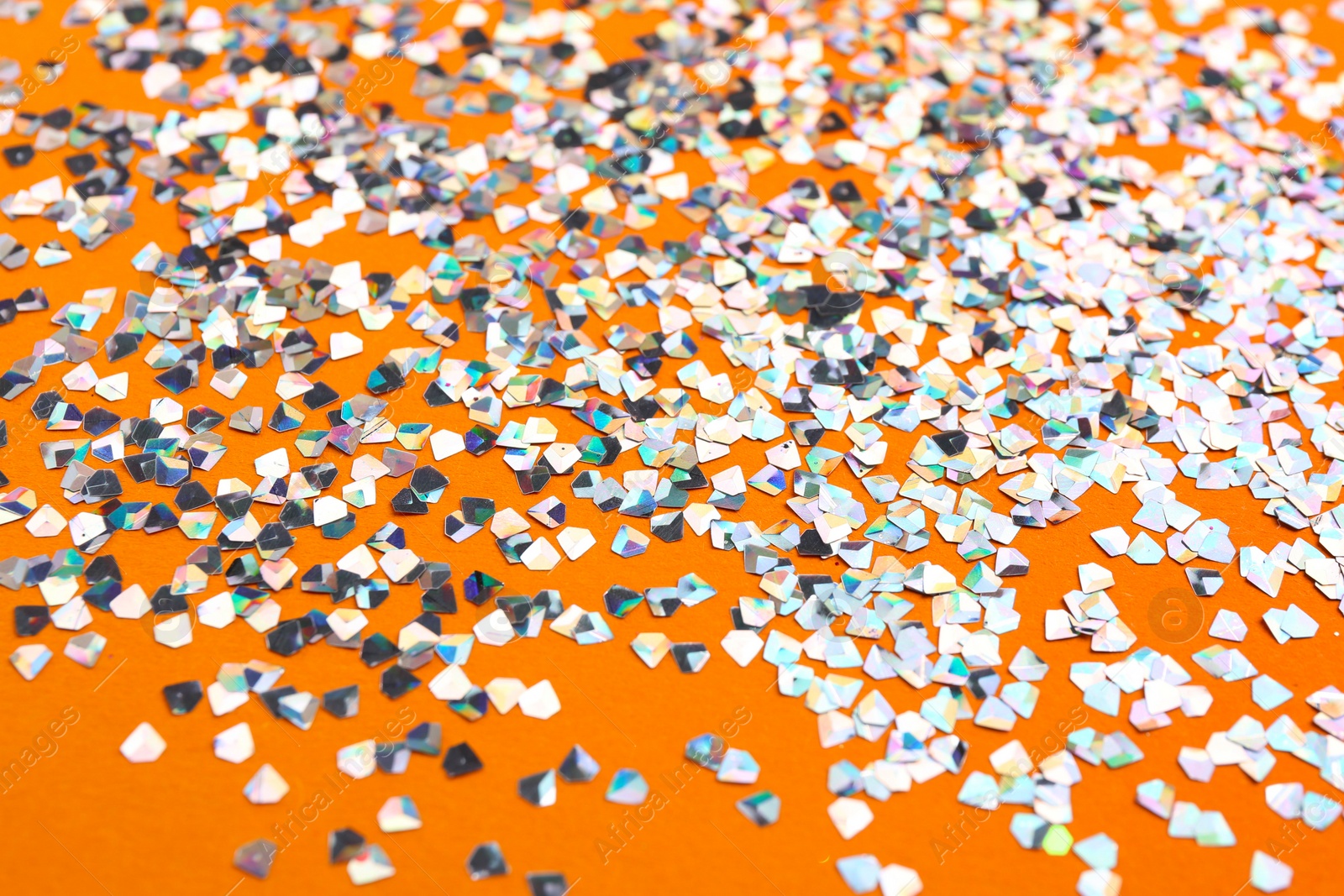 Photo of Shiny bright glitter scattered on orange background