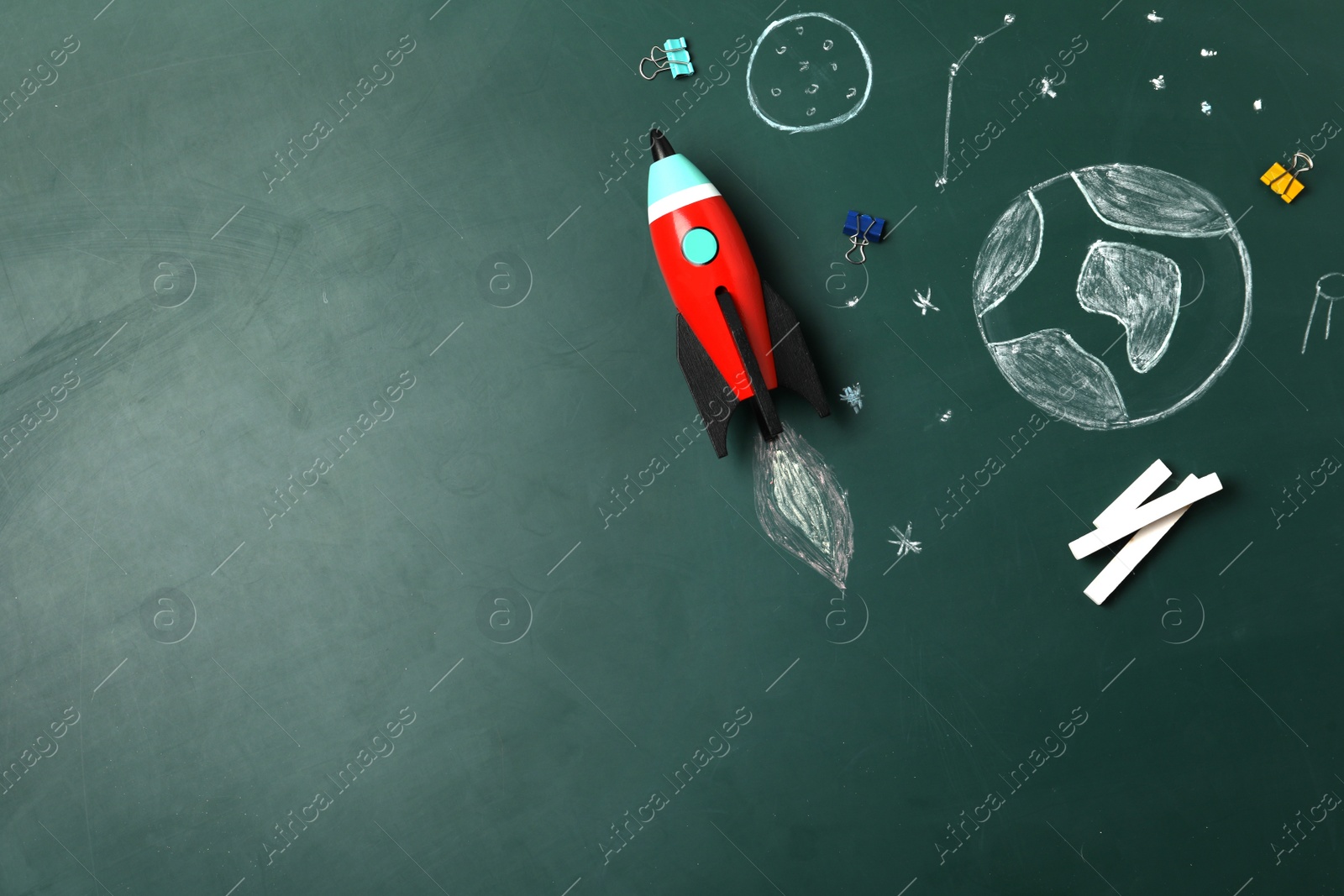 Photo of Bright toy rocket, school supplies and drawings on chalkboard, flat lay. Space for text