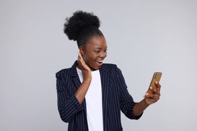 Happy young woman using smartphone on light grey background