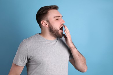 Photo of Sleepy young man yawning on light blue background