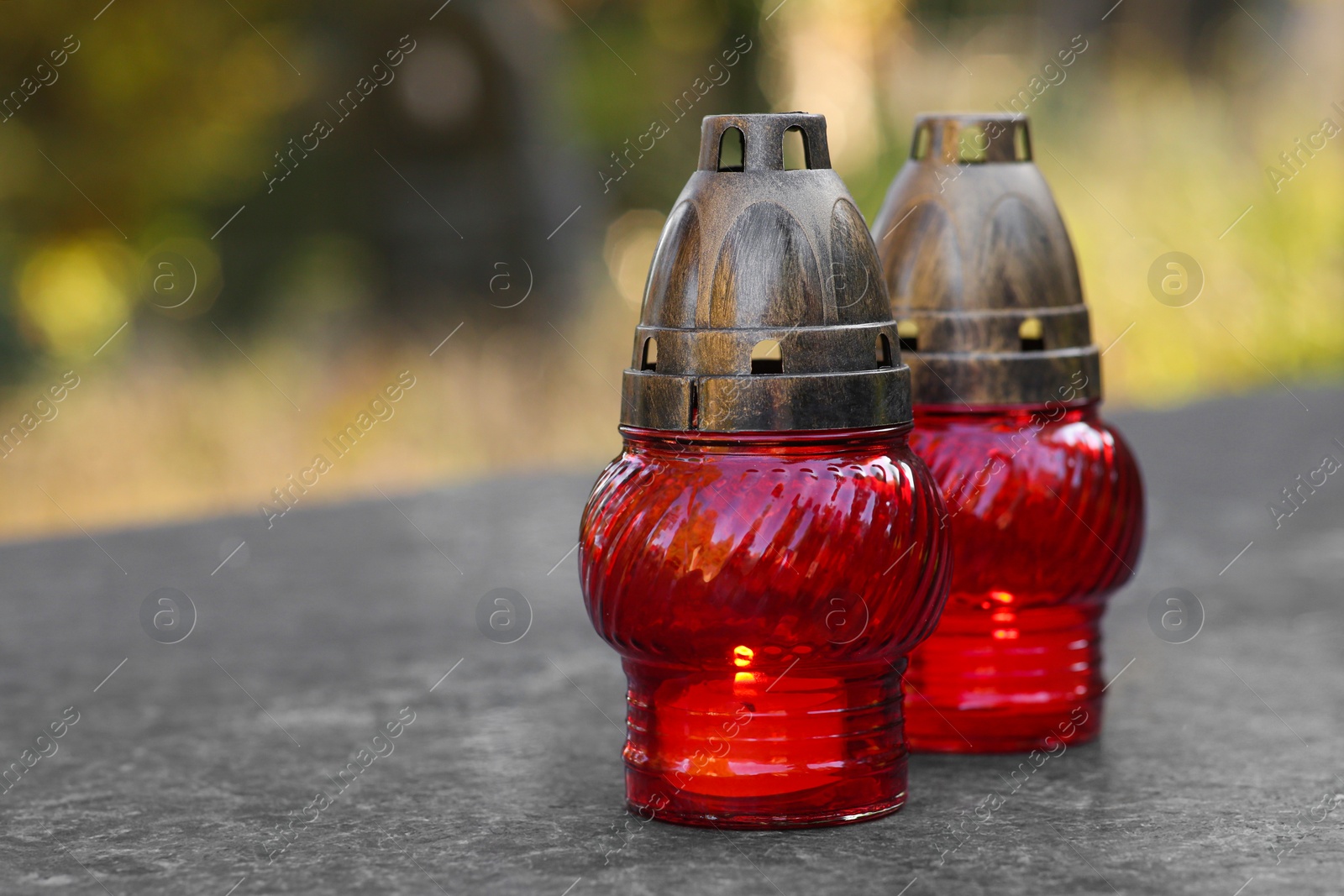 Photo of Red grave lanterns with burning candles on granite surface in cemetery, space for text