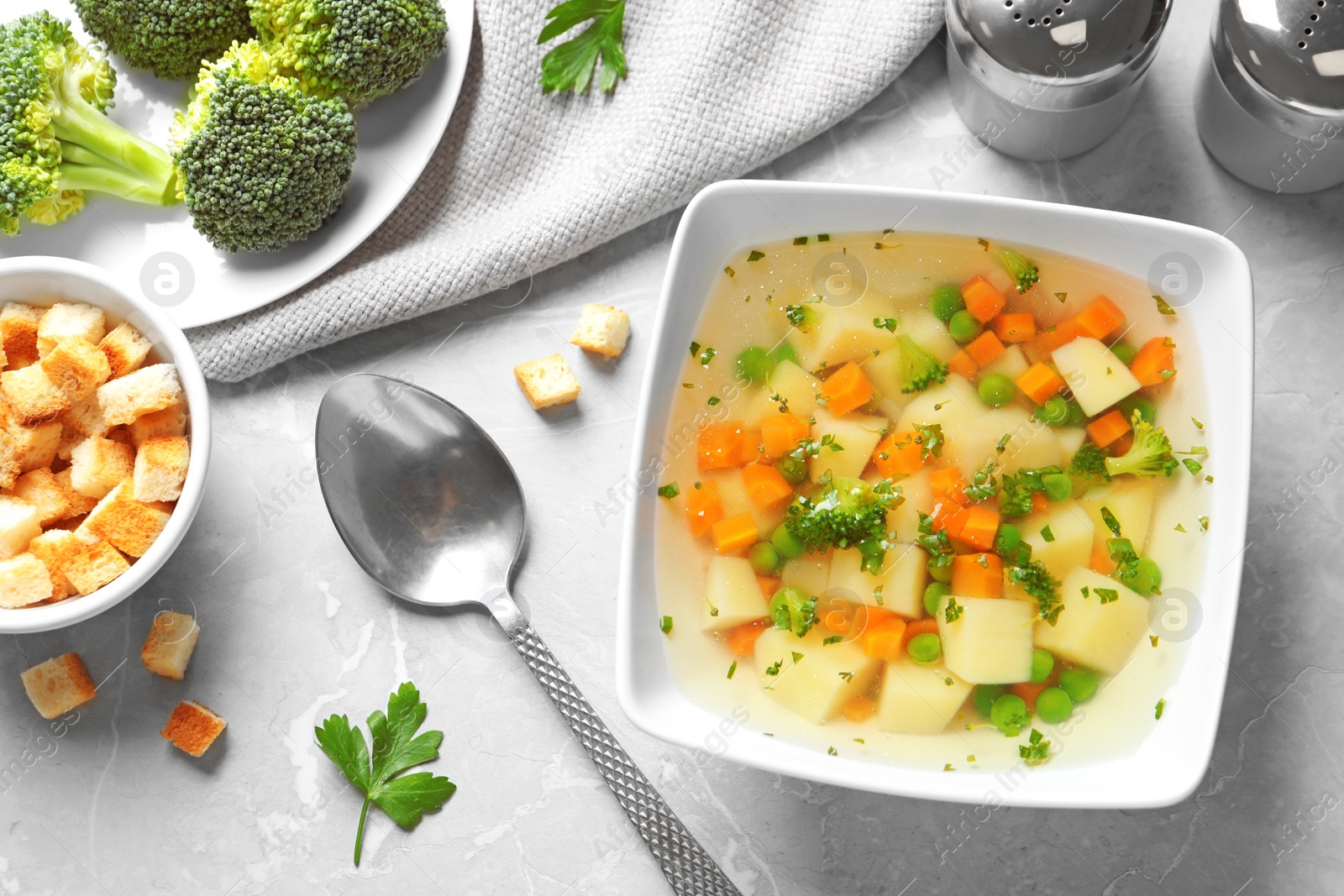 Photo of Bowl of fresh homemade vegetable soup served on grey marble table, flat lay