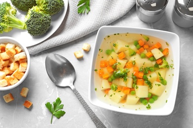 Bowl of fresh homemade vegetable soup served on grey marble table, flat lay