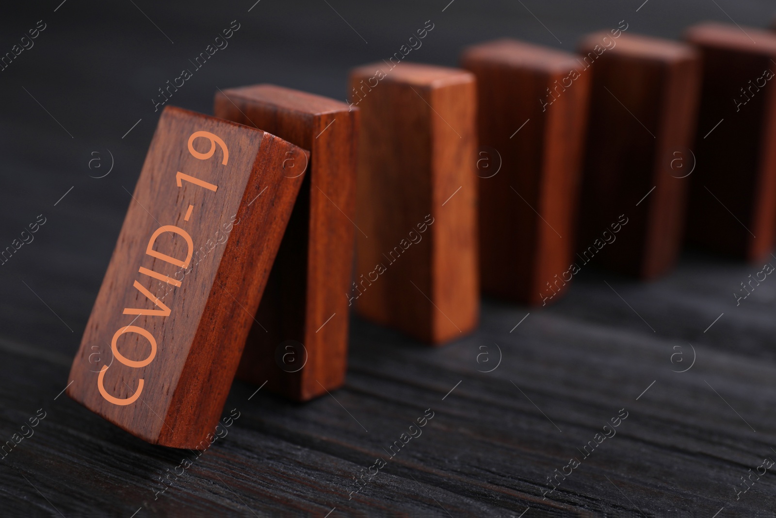 Photo of Falling wooden domino tiles on black table, closeup. Spreading of coronavirus concept