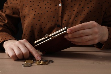 Poverty. Woman with wallet counting coins at wooden table, closeup