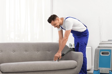 Dry cleaning worker removing dirt from sofa indoors