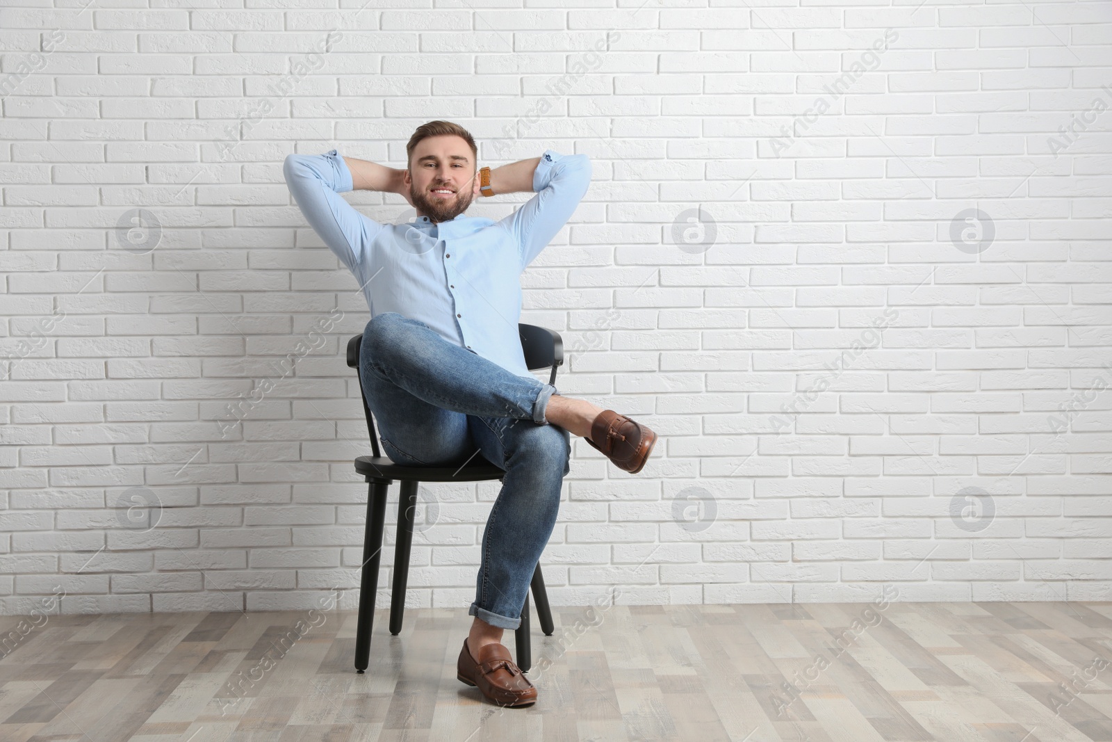 Photo of Young man relaxing on chair near white brick wall in office, space for text