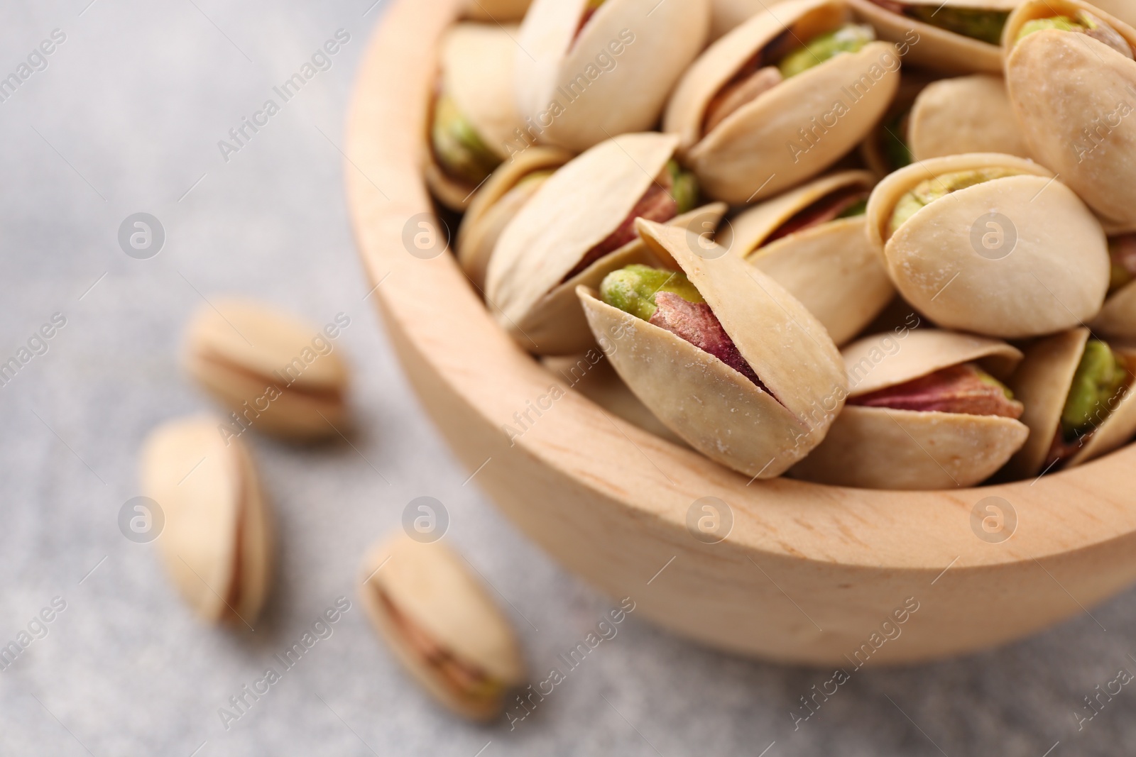 Photo of Delicious pistachios in bowl on grey textured table, closeup