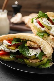 Photo of Delicious pita sandwiches with grilled vegetables and sour cream sauce on black table, closeup