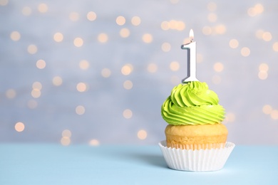 Photo of Birthday cupcake with number one candle on table against festive lights, space for text