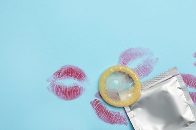 Photo of Condom with lipstick kiss marks and space for text on light blue background, flat lay. Safe sex