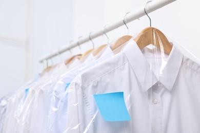 Photo of Dry-cleaning service. Many different clothes in plastic bags hanging on rack against white background, closeup