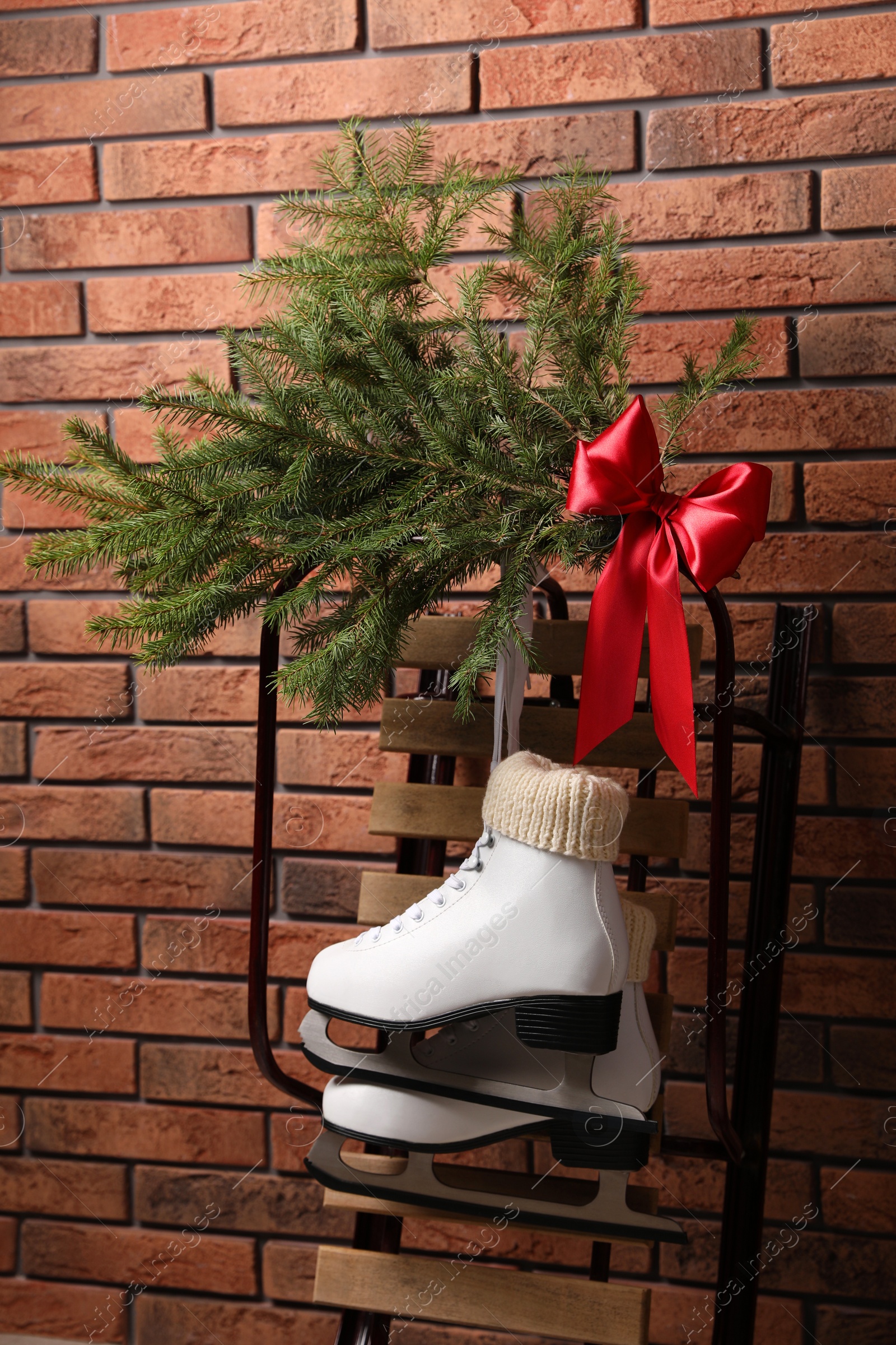 Photo of Sleigh with pair of ice skates and fir branches near brick wall