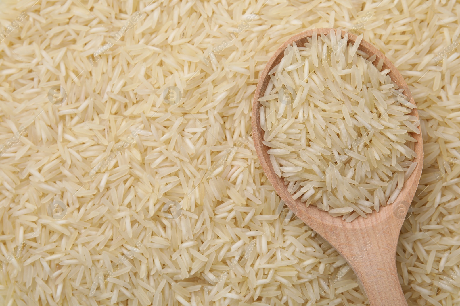 Photo of Wooden spoon and raw rice as background, top view. Space for text