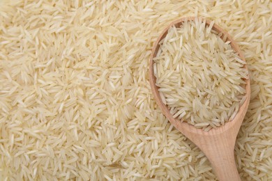 Photo of Wooden spoon and raw rice as background, top view. Space for text