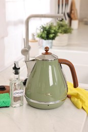 Cleaning electric kettle. Bottle of vinegar, sponge and rubber glove on countertop in kitchen