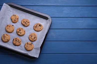 Baking pan with cookies and parchment paper on blue wooden table, top view. Space for text