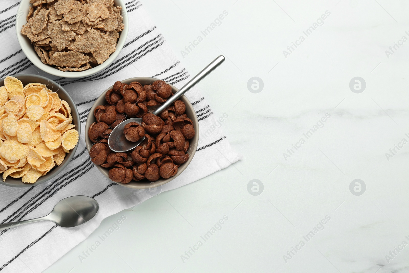 Photo of Different delicious breakfast cereals on white table, flat lay. Space for text