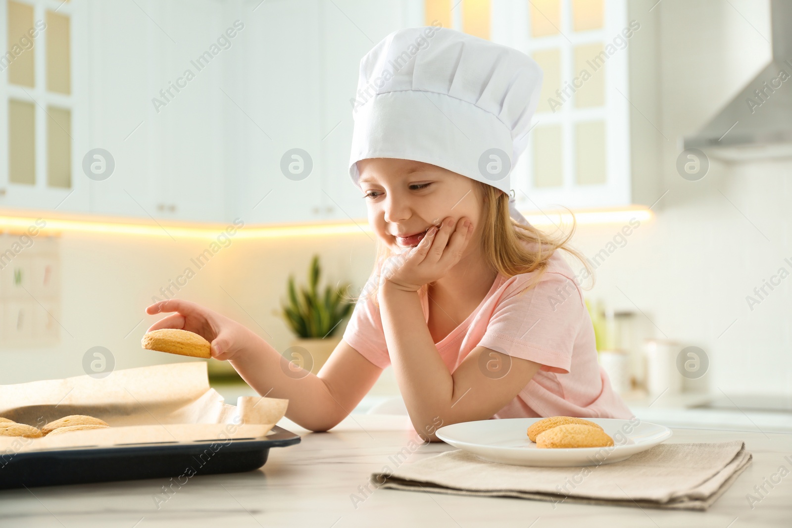 Photo of Little girl wearing chef hat baking cookies in kitchen