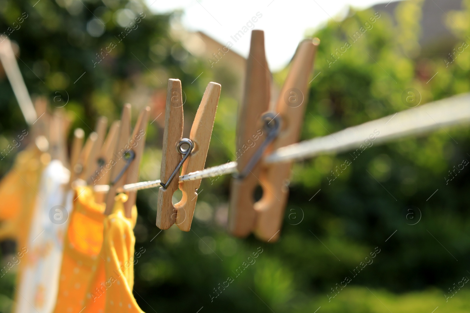 Photo of Clean clothes drying outdoors during sunny day, focus on laundry line with wooden clothespins