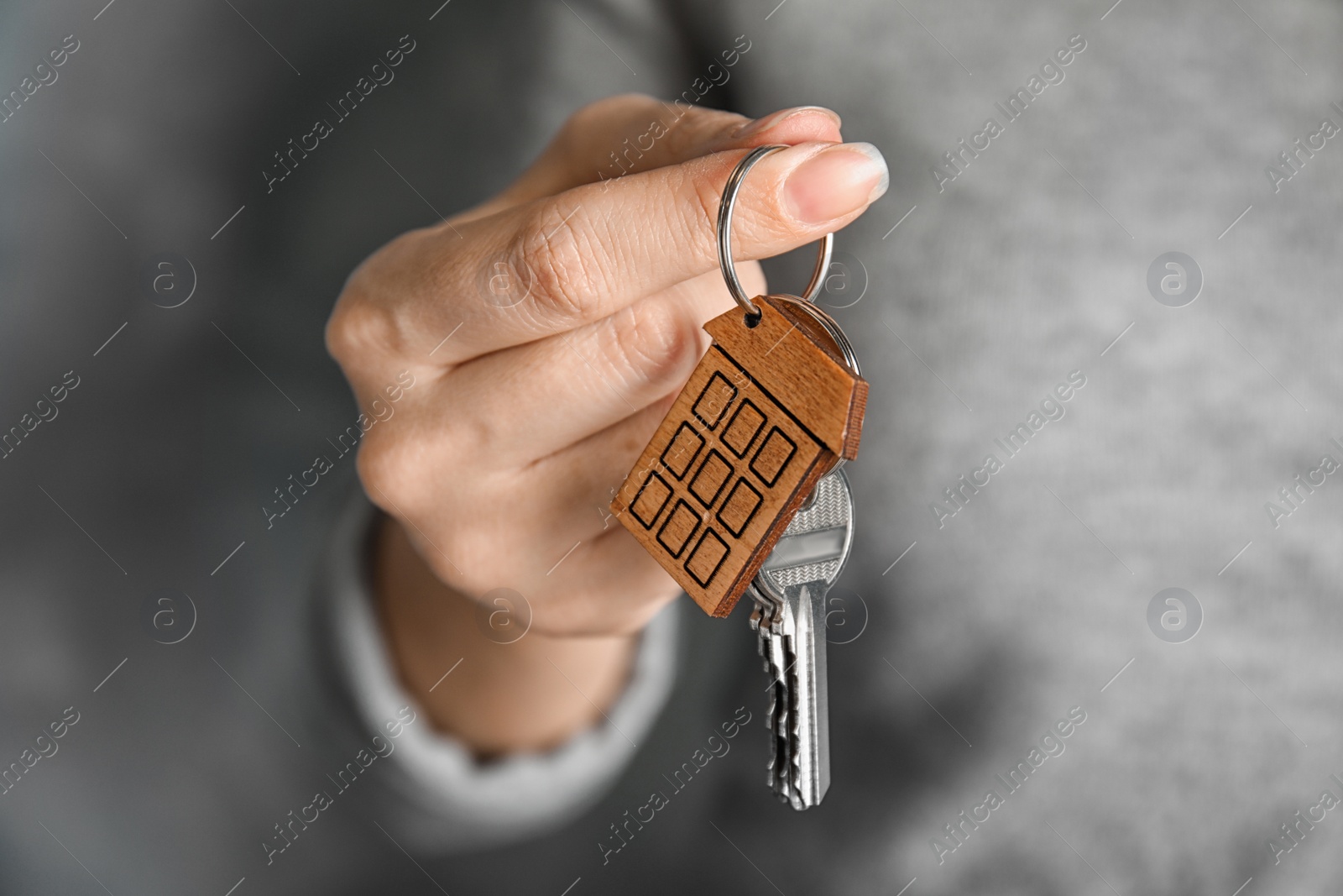 Photo of Woman holding house key with trinket on blurred background, closeup