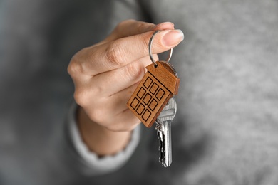 Photo of Woman holding house key with trinket on blurred background, closeup