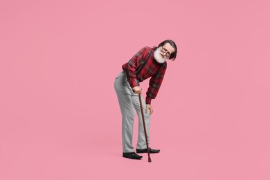 Photo of Tired senior man with walking cane suffering from knee pain on pink background