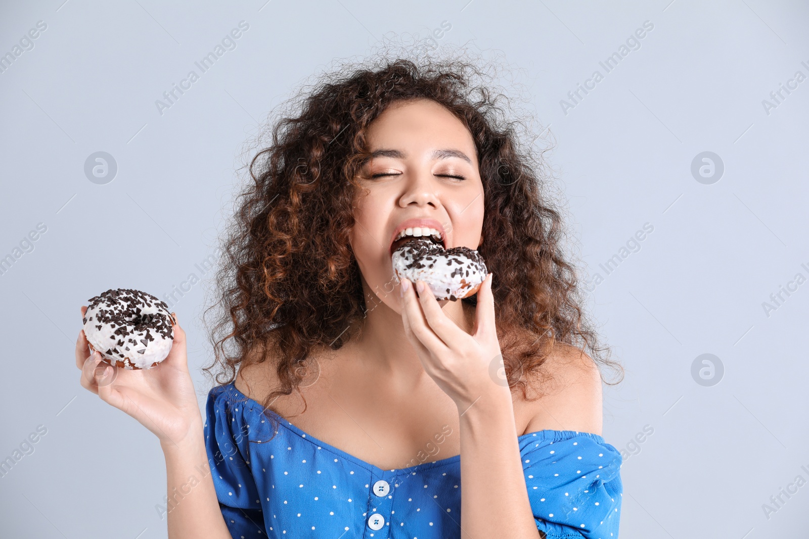 Photo of Beautiful African-American woman with donuts on light grey background