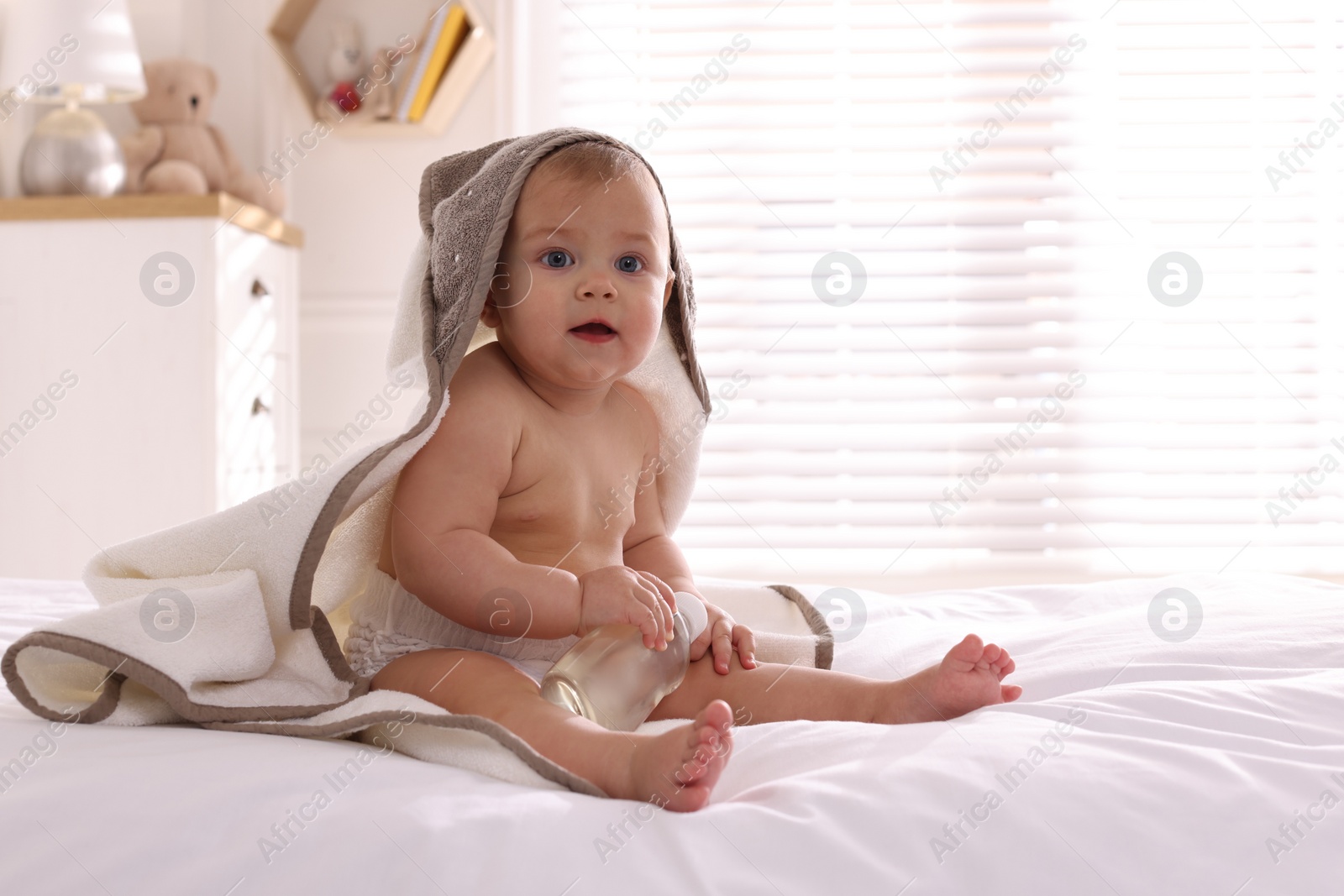 Photo of Cute little baby with towel and bottle of massage oil on bed at home