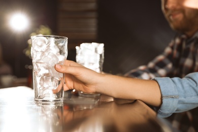 Woman holding glass with ice cubes for cola at bar counter