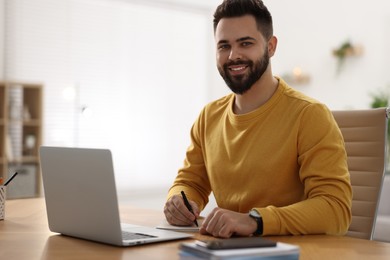 Photo of Young man watching webinar at table in room