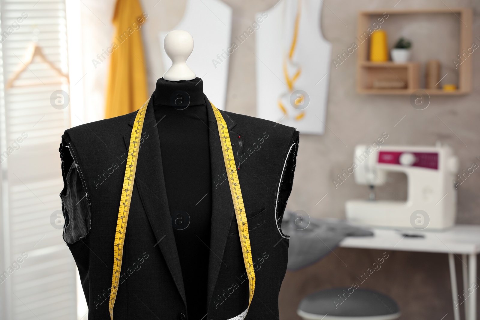 Photo of Mannequin with unfinished suit jacket and measuring tape in tailor shop. Space for text