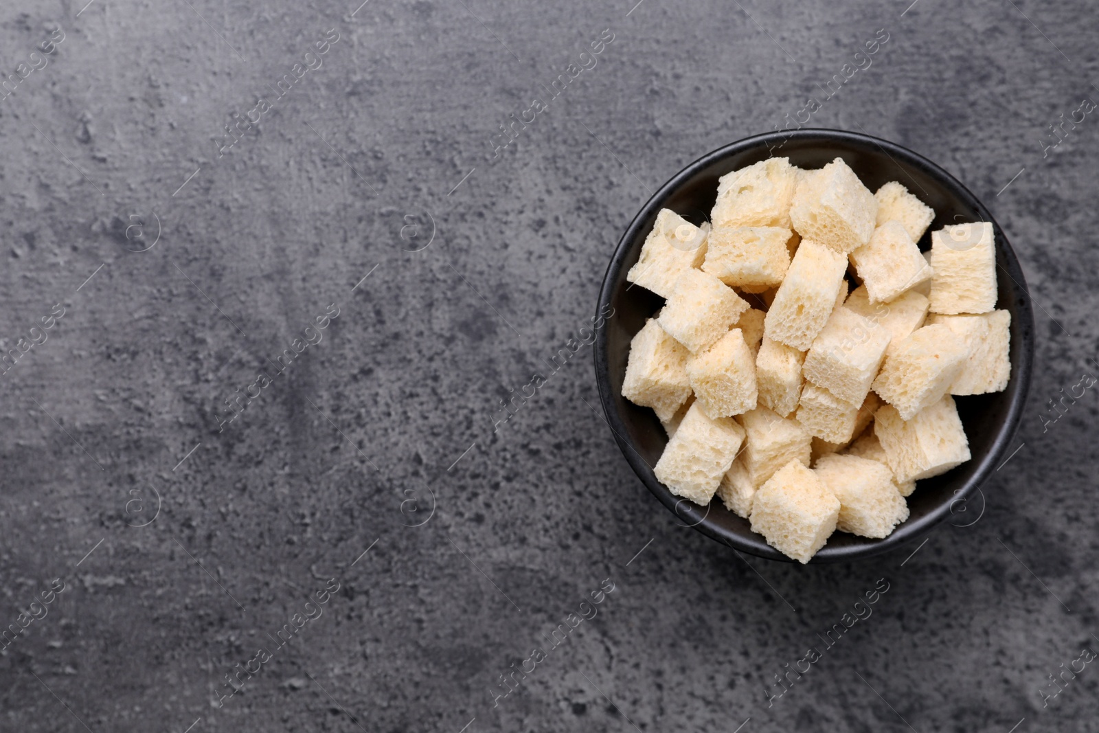 Photo of Crispy rusks in bowl on grey table, top view. Space for text