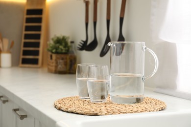 Jug and glasses with clear water on white table in kitchen, space for text