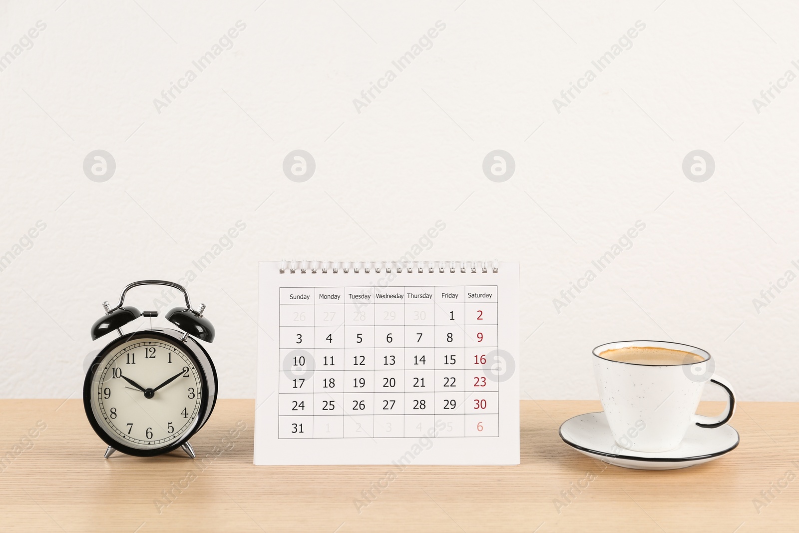 Photo of Calendar, alarm clock and cup of coffee on wooden table