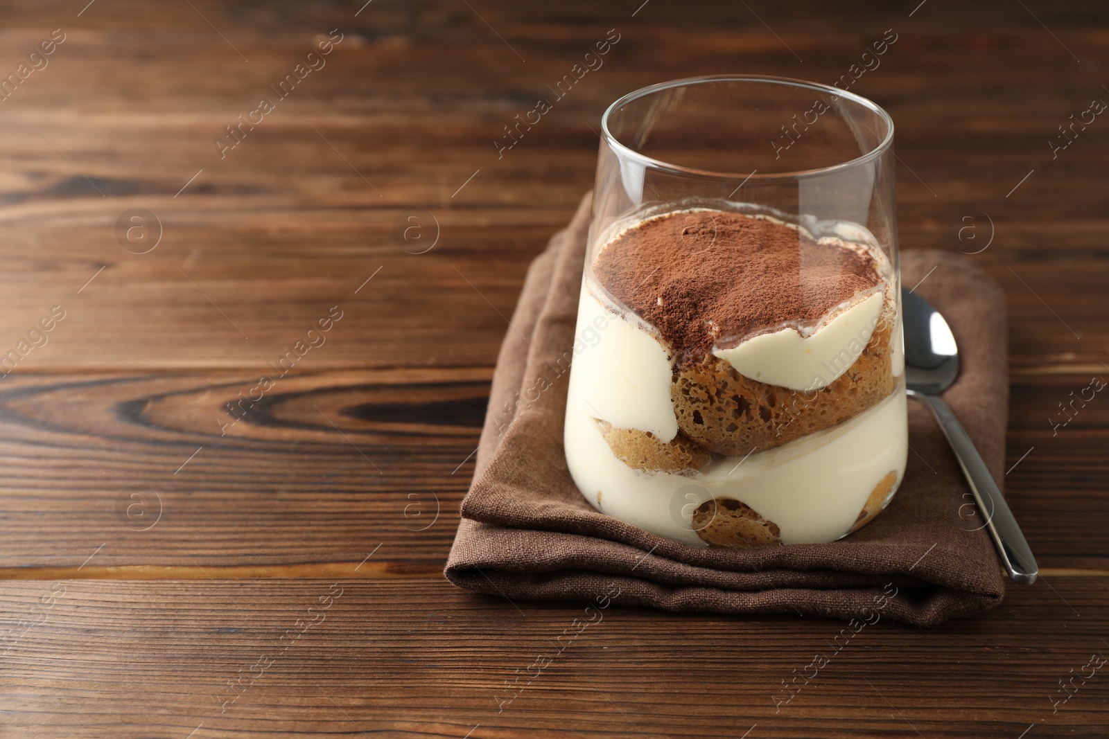 Photo of Delicious tiramisu in glass and spoon on wooden table. Space for text